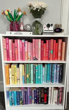 a bookshelf filled with lots of colorful books next to a vase full of flowers