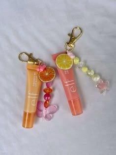 two lip glosses and a keychain on a white sheet with some fruit