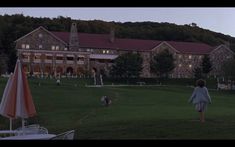 a woman walking across a lush green field in front of a large building at dusk