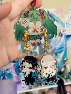 two keychains with anime characters on them in front of a shelf full of other items