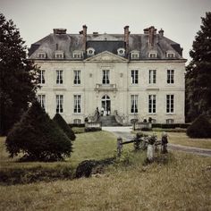 a large white building sitting in the middle of a lush green field next to trees