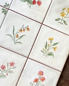 four tiles with flowers painted on them are sitting on the floor next to each other