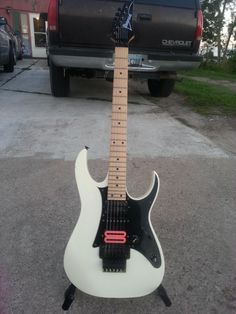 an electric guitar sitting on top of a stand in front of a black pickup truck