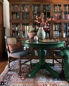 a green table with chairs around it in front of a bookcase filled with books