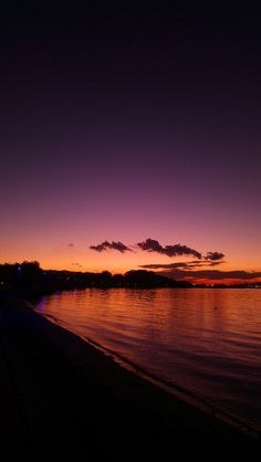 the sky is purple and orange as the sun sets on the water's edge