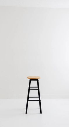 a black stool with a wooden seat in front of a plain white wall and floor