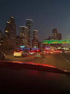 the city skyline is lit up at night as cars drive down the highway in front of them