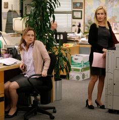 two women standing in an office area with desks and filing cabinets on either side