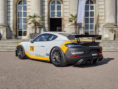 a white and yellow sports car parked in front of a large building with steps leading up to it