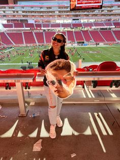a woman standing next to a young boy in front of a football stadium filled with fans