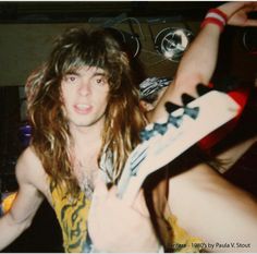 a young man with long hair holding a guitar in his right hand and looking at the camera