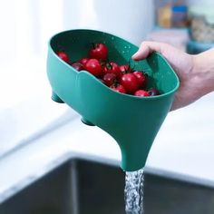 a person holding a green strainer over a sink filled with cherries and water