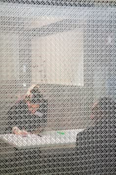 two people sitting at a table in front of a window with white mesh covering them