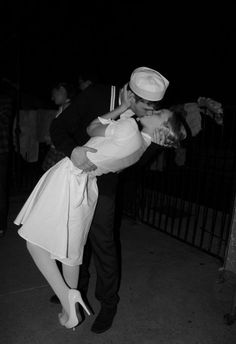 a sailor kissing a woman on the cheek while she is dressed in white and black