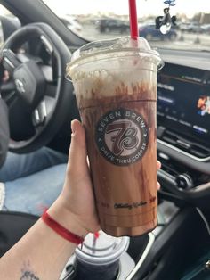 a person holding up a cup of coffee in their hand with the steering wheel behind them