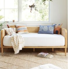 a white couch sitting under a window in a living room next to a rug and pillows
