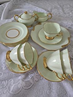 a table topped with lots of white and gold china dishes on top of a lace covered table cloth