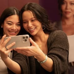 two women are taking a selfie with their cell phone in front of them and smiling