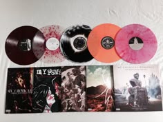 five different colored vinyl records on a white surface next to two orange and one pink discs