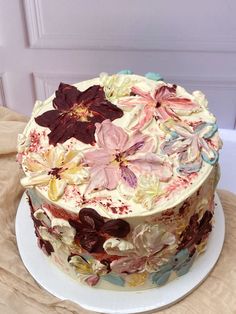 a cake with flowers on it sitting on a table next to a white plate and brown cloth