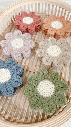 four crocheted flowers sitting on top of a wicker basket next to each other