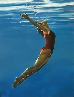 a woman in a red and gold swimsuit dives underwater with her hands above the water's surface