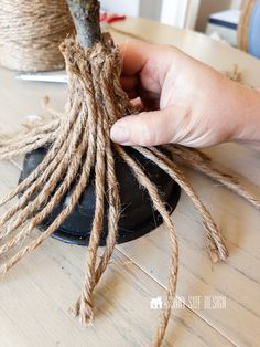 someone is tying up some twine to a tree branch on a wooden table in front of a potted plant