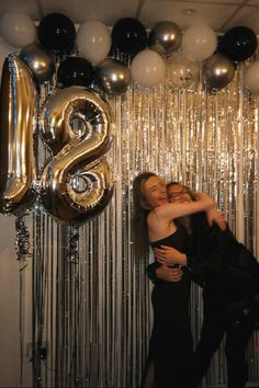 two women hugging each other in front of balloons and streamers with the number 8 on it