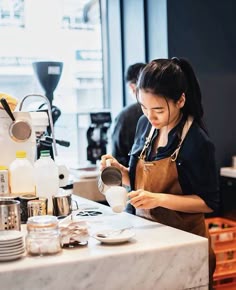 a woman in an apron is pouring something into a cup at a counter with other coffee cups