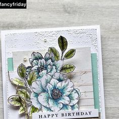 a handmade birthday card with blue flowers and green leaves on the front, sitting on a wooden surface