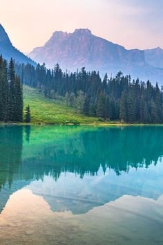 a lake surrounded by mountains and trees with blue water in the foreground on a cloudy day