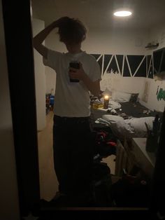 a person standing in a room holding a cell phone and looking at his reflection on the mirror