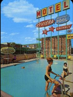 two women in bathing suits standing by the edge of a swimming pool, with motels and neon signs behind them