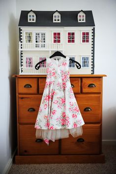 a doll house on top of a dresser next to a dress hanging from it's hanger