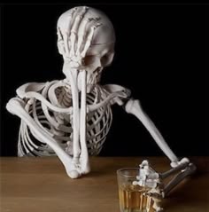 a skeleton sitting next to a glass of whiskey