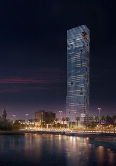a very tall building sitting on the side of a body of water in front of a city at night