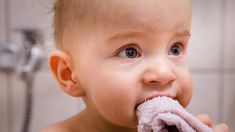 a baby is brushing his teeth in the bathtub while holding a towel over its mouth