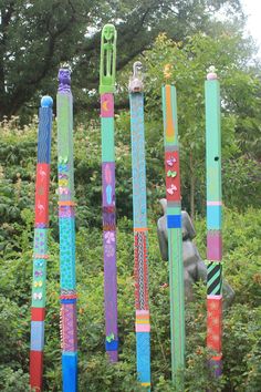 a bunch of different colored sticks hanging in the air next to some bushes and trees