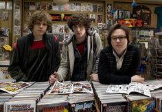 three young men sitting at a table covered in comic books