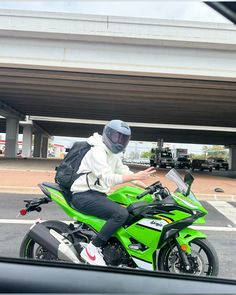 a man riding on the back of a green motorcycle in a parking lot next to an overpass