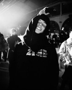 a man in a hoodie is smiling at the camera while other people stand around him