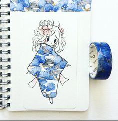 a spiral notebook with a drawing of a woman wearing a blue kimono next to a roll of washi tape