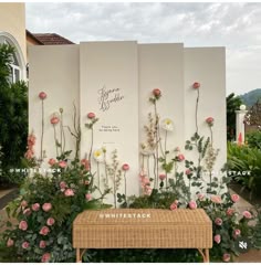 a bench sitting in front of a white wall with pink flowers and greenery on it