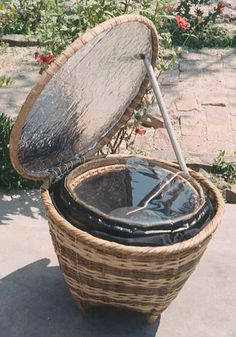 an old woven basket with a metal lid sitting on the ground next to some flowers