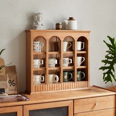 a wooden cabinet filled with lots of cups and saucers next to a potted plant