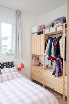 a bedroom with a bed, dresser and clothes hanging on the shelves in front of the window