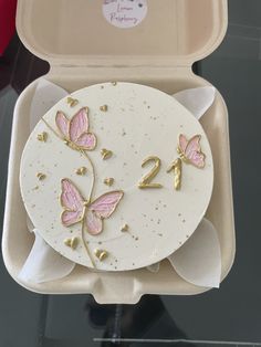 a cake in a box decorated with pink and gold butterflies on the front, number two