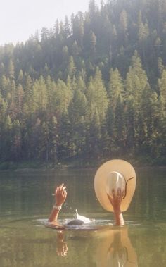 a person floating in the water with a hat on their head and one hand reaching out for something