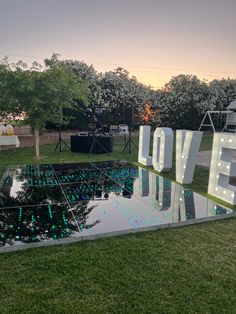 the word love spelled out in front of a pond with lights on it at sunset