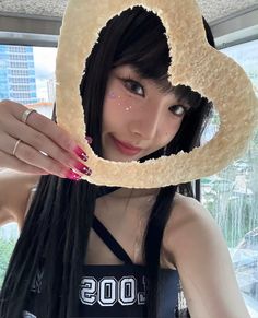 a woman with long black hair holding up a doughnut shaped like a heart